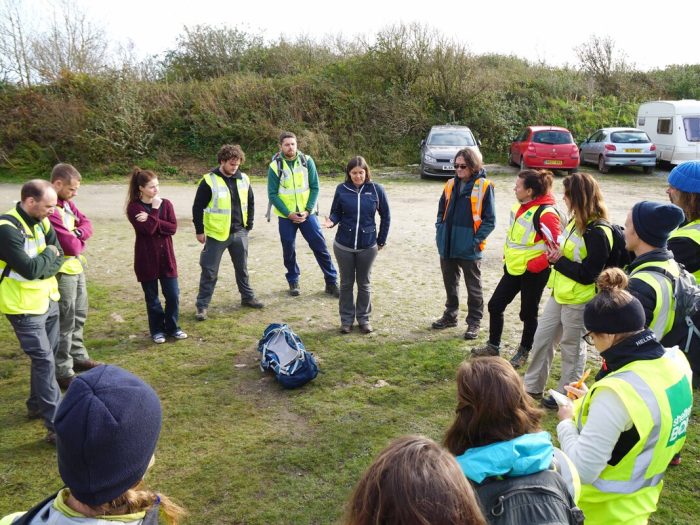 People in high vis vests standing around a speaker outside