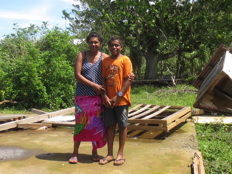 Woman and boy standing in destroyed house in Fiji