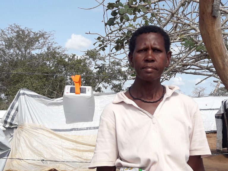 Woman standing in front of tents and next to a solar light in Kenya