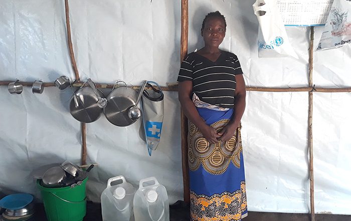 Woman standing in a shelter in Malawi next to household items
