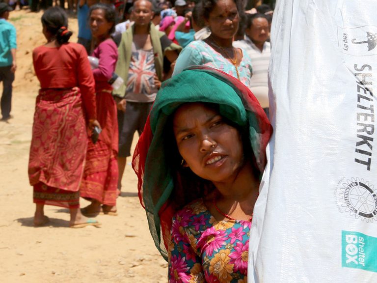Woman carrying a shelter kit in front of crowds in Nepal