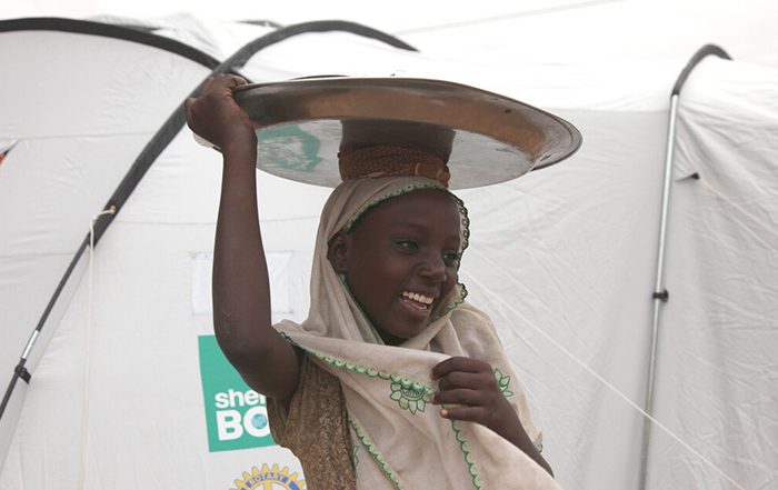 Girls carrying item on her head outside a tent in Niger