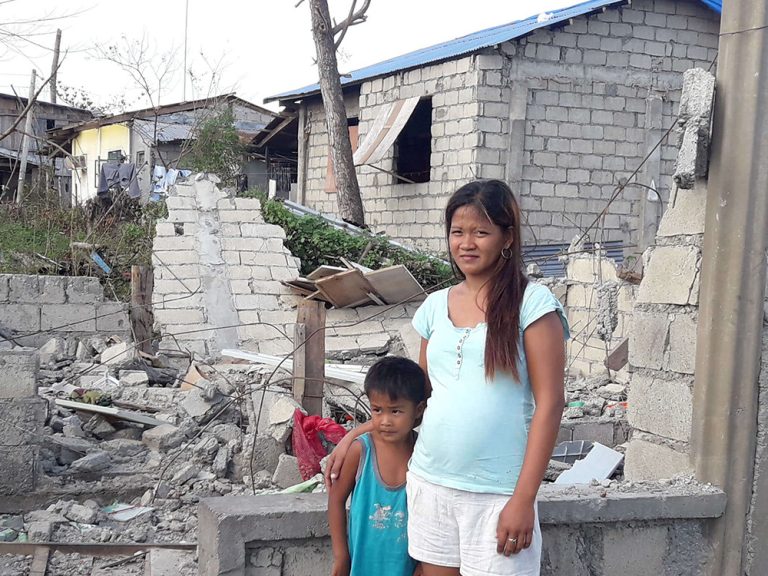 Woman and boy standing in remains of damaged home in the Philippines
