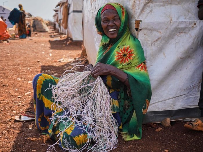 Woman sitting next to a tent and weaving fibres in Somalia