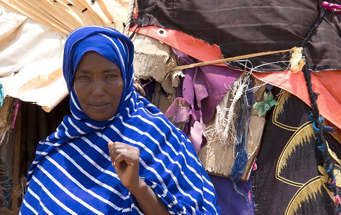 Woman wearing a blue and white striped headscarf in front of shelter in Somaliland