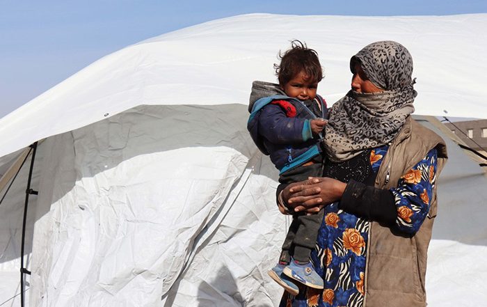 Woman holding a child outside a tent in Syria
