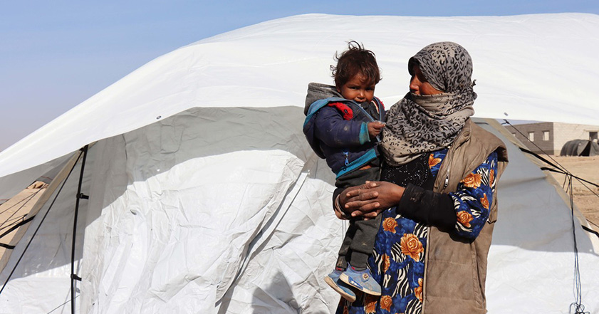 Woman holding a child outside a tent in Syria