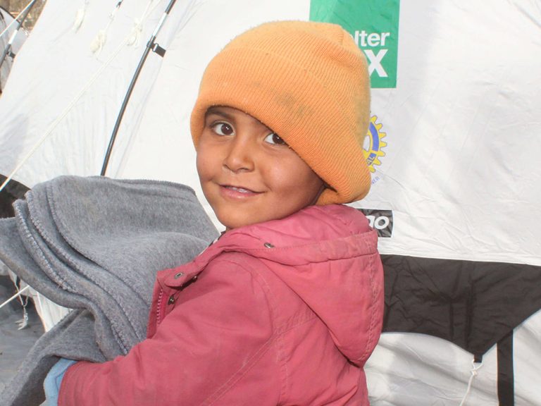Young child holding a blanket outside a tent in Syria