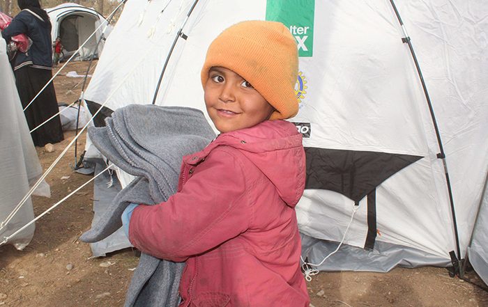 Little girl holding a blanket outside a ShelterBox tent in Syria
