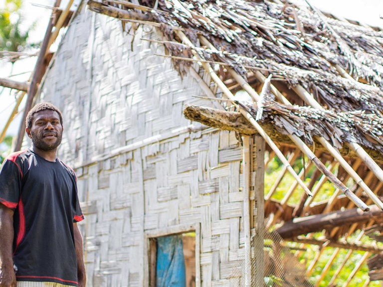 Man standing outside a building damaged by a cyclone in Vanuatu