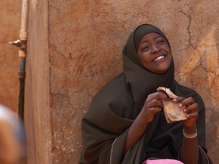 Woman sitting smiling next to a shelter in Somalia