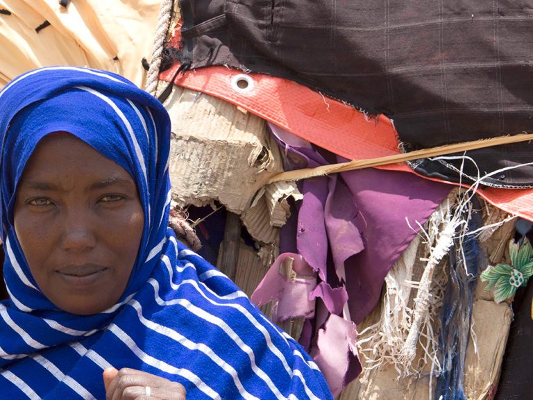 Woman wearing blue and white striped headscarf in front of a shelter in Somaliland
