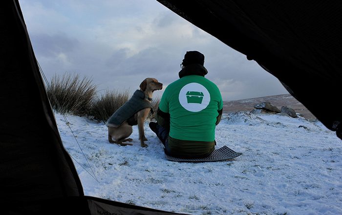 Man sitting in the snow with his dog outside a tent