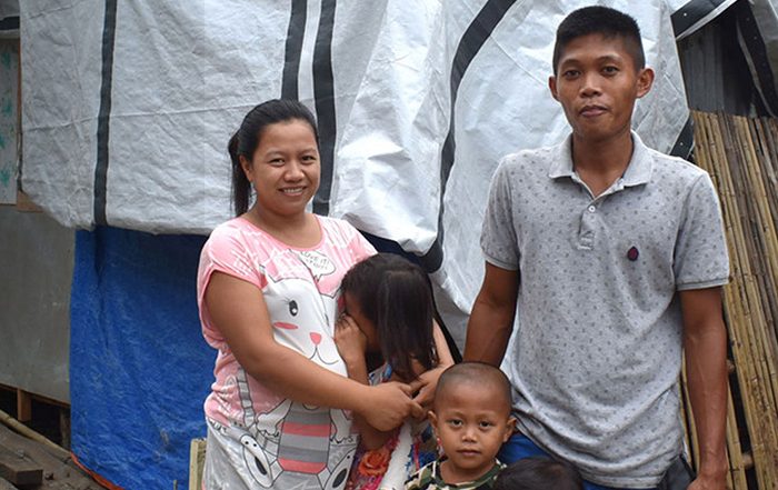 Family outside a home repaired with a tarpaulin in the Philippines