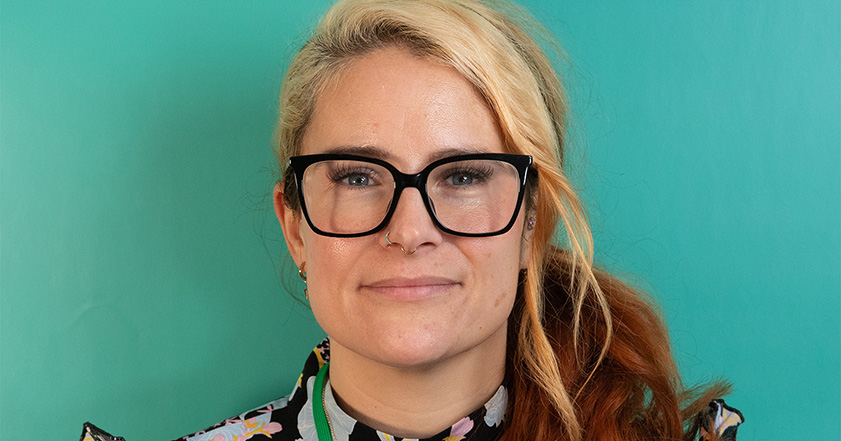 Woman with blond and brown hair wearing glasses against a green background