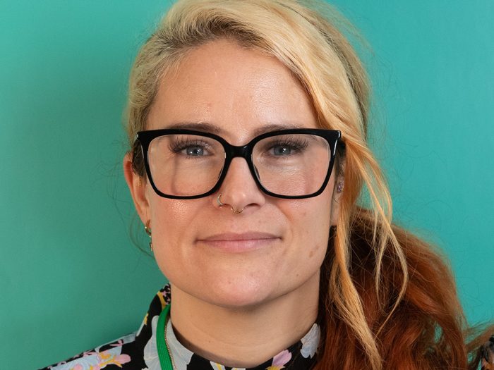 Portrait photo of woman wearing glasses with brown and blonde hair against a green background