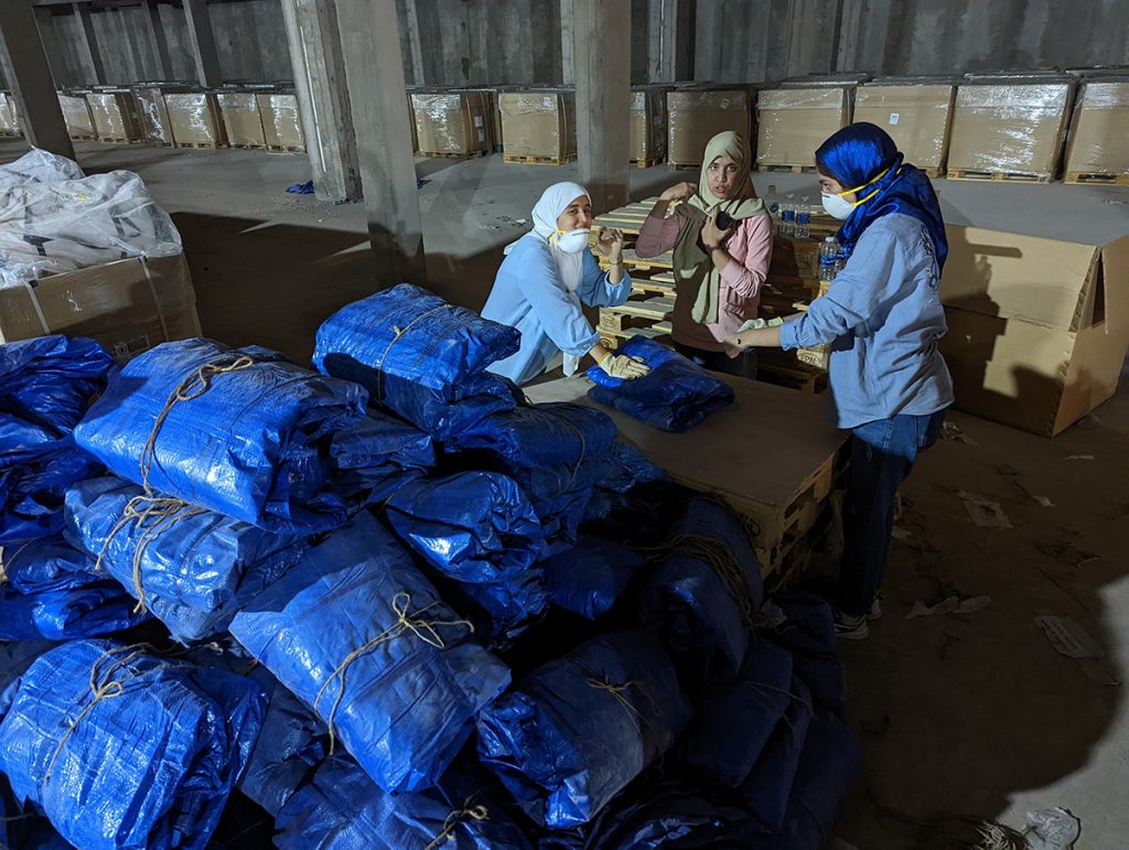 Three women tying up blue wrappers of aid materials ready for reuse in Morocco