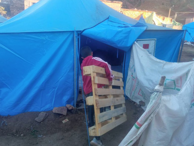 Boy taking wooden pallet into a tent in Morocco