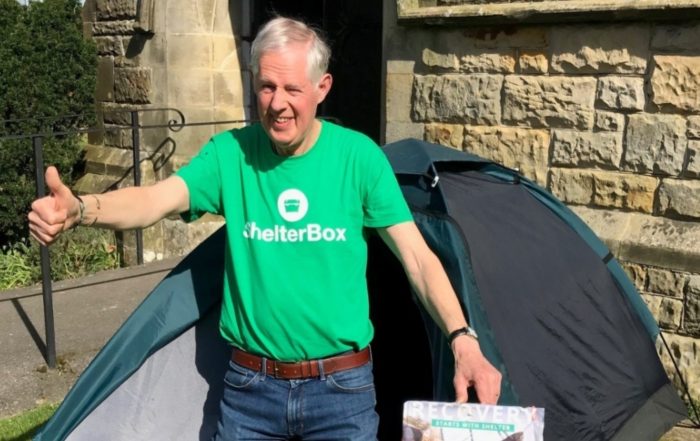 Man wearing a ShelterBox t-shirt outside a tent