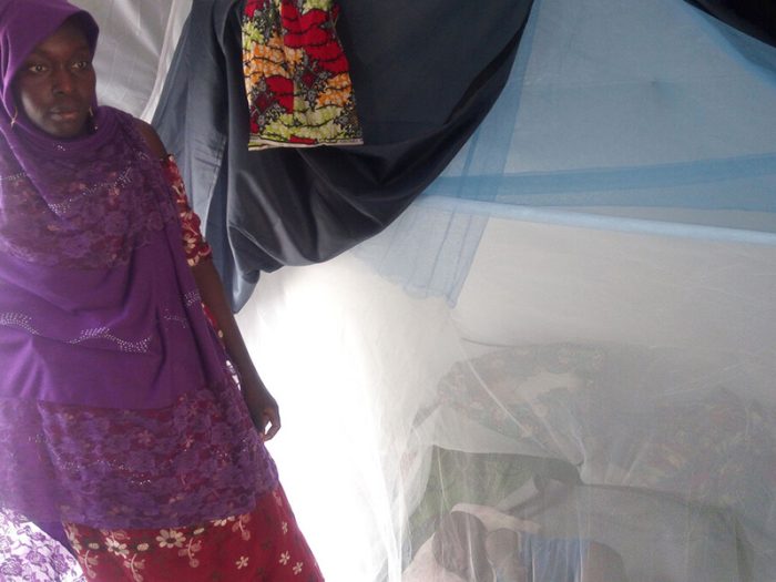 Woman in a tent with her baby asleep under a mosquito net behind