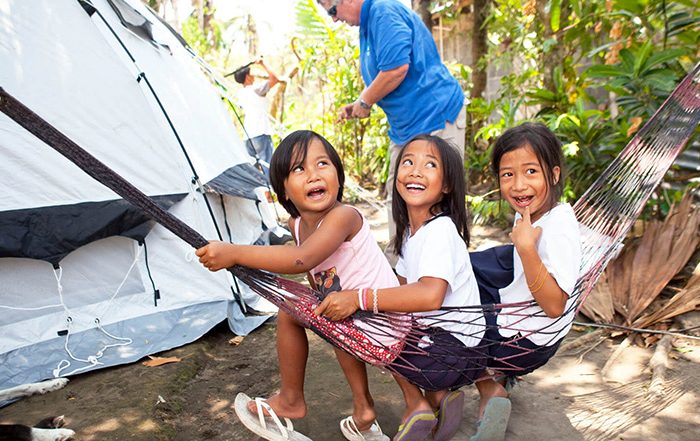 3 children sitting in a hammock next to a tent in the Philippines