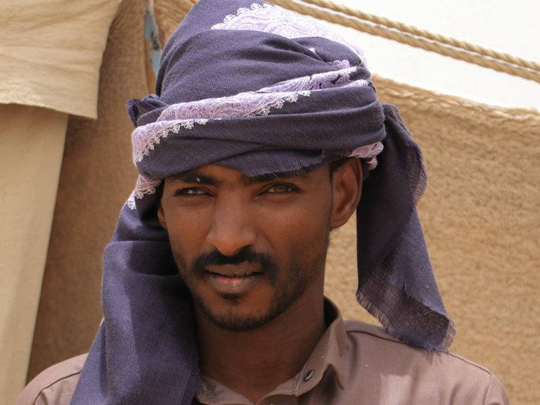 Man wearing purple head turban outside a shelter in Yemen