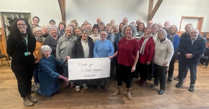The Inglehart Singers, and Community Fundraising Officer, Louisa Arnold, stand together with a cheque for £1000. Money raised by the choir for ShelterBox during 2023.