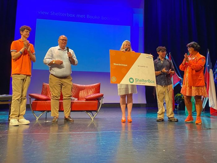 5 people standing on a stage, one holding a large piece of cardboard