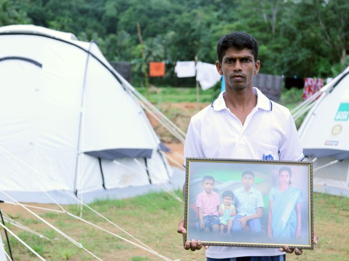 Man holding picture of his wife and 3 children among tents in Sri Lanka