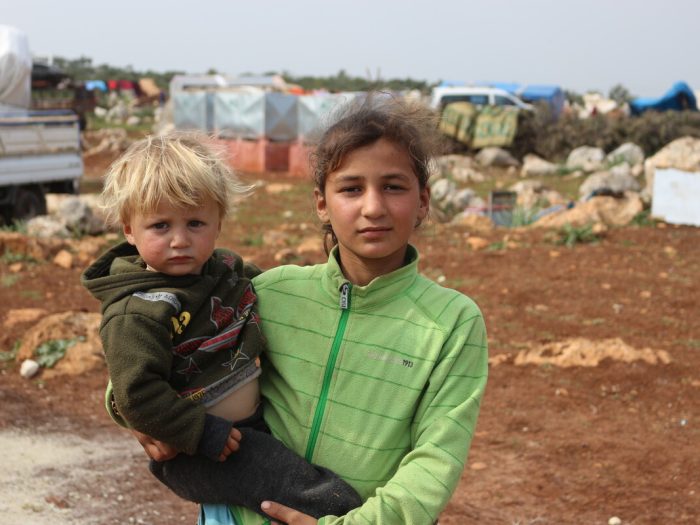 Girl in green holding a little child in a Syria displacement camp