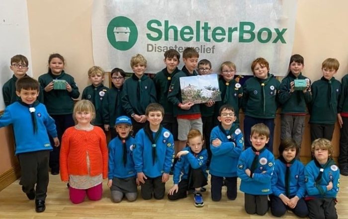A group of children standing and kneeing in front of a ShelterBox banner