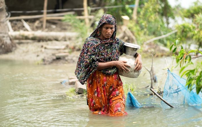 A lady walks through knee high water carrying a pot