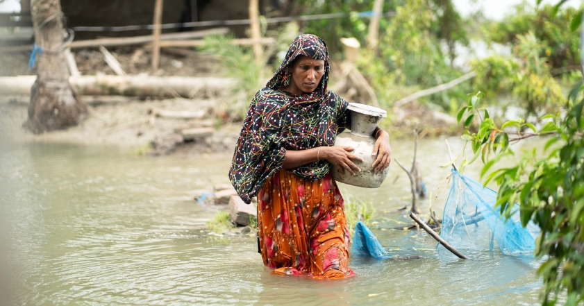 A lady walks through knee high water carrying a pot