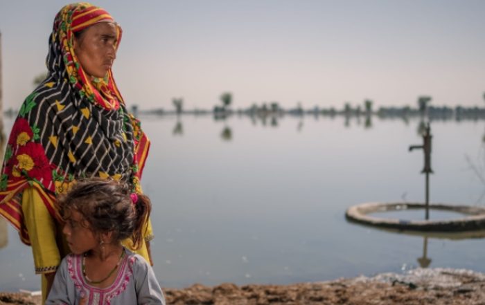 A woman wearing a headscarf and a young girl stand infront of a large area of flooded land