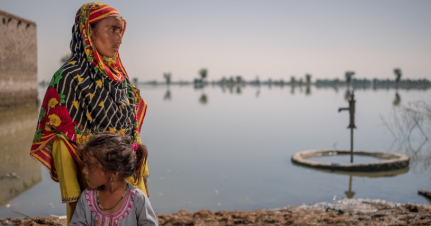 A woman wearing a headscarf and a young girl stand infront of a large area of flooded land