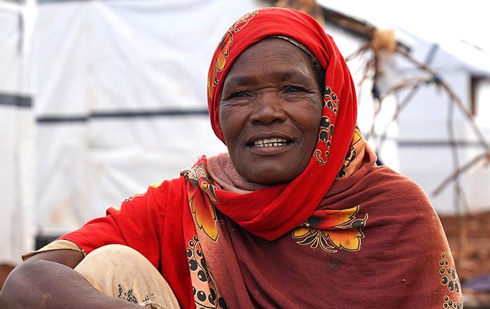 Woman in bright red head scarf sitting in front of shelters in Somalia