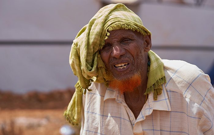 Man wearing green head scarf and white shirt in front of shelters in Somalia