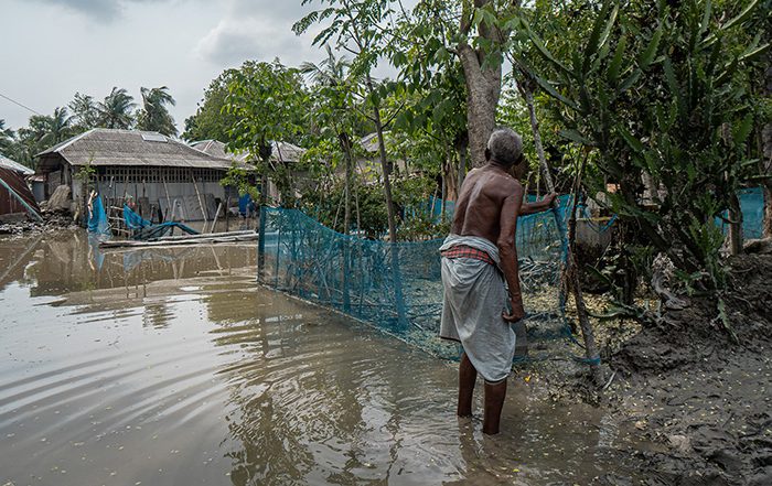 Man in floodwater next to damaged homes in Bangladesh