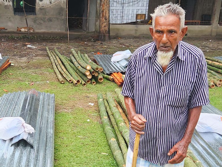 Elderly man standing next to piles of wood and metal in Bangladesh