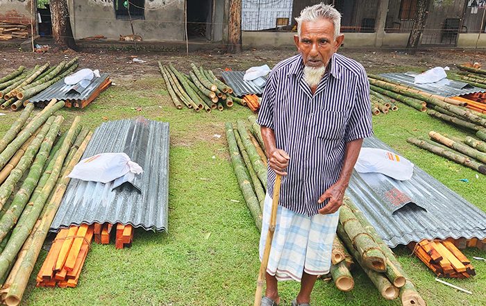 Elderly man standing next to piles of metal and wood in Bangladesh