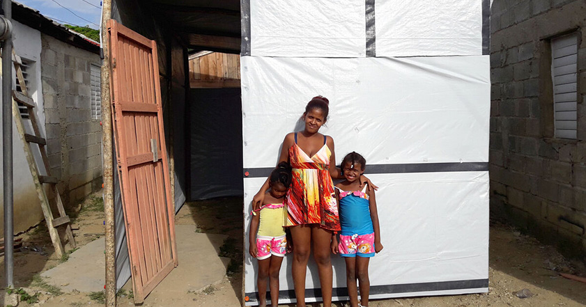 Woman and two children standing outside a shelter made of tarpaulins in the Caribbean