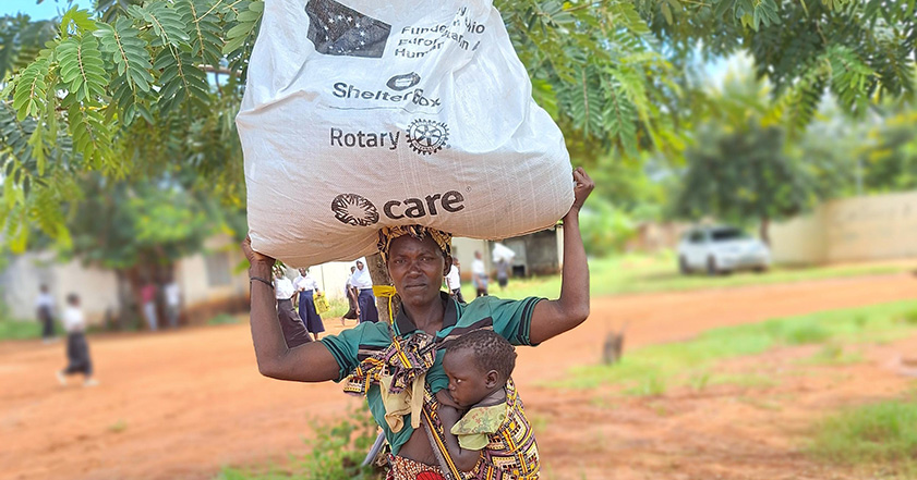 Woman carrying a bag of aid on her head while breastfeeding a baby in Mozambique