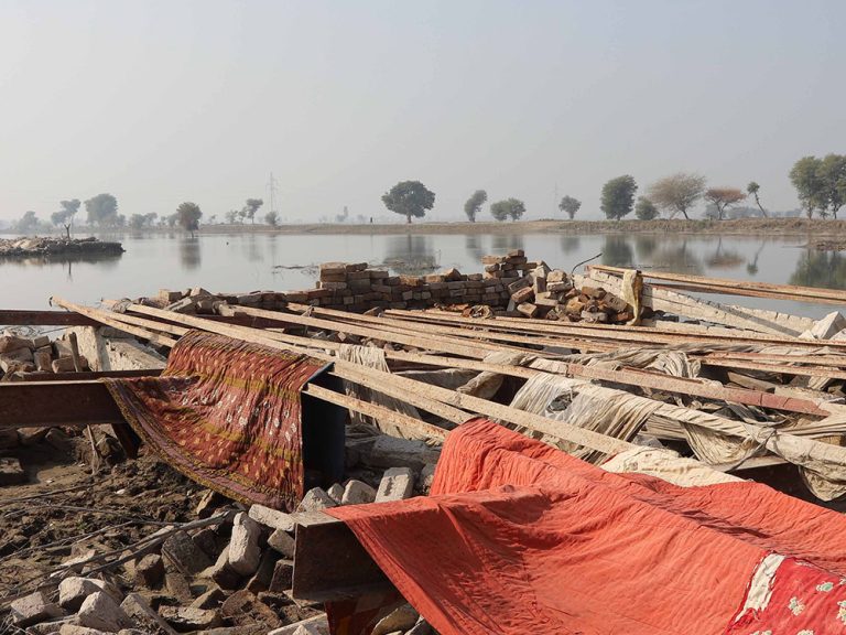 Flooded landscape next to rubble and cloths laid out to dry in Pakistan