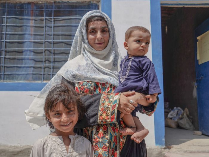 Woman holding a child next to another child outside a home in Pakistan