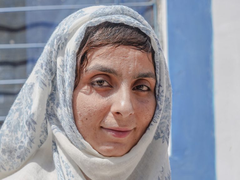 Woman wearing white and blue headscarf smiling at the camera