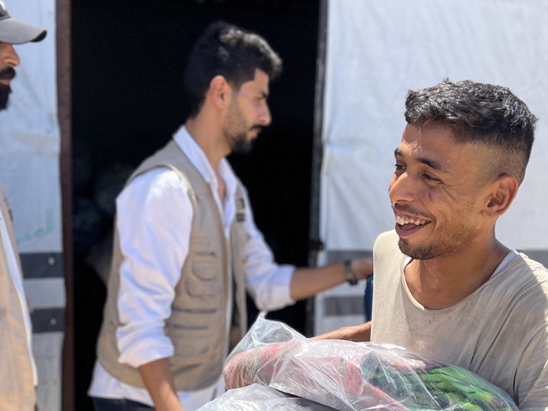 Man smiling while holding aid collected from outside a tent in Gaza