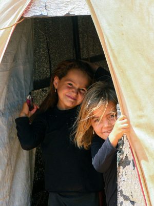 two girls peek out from behind a tent in syria