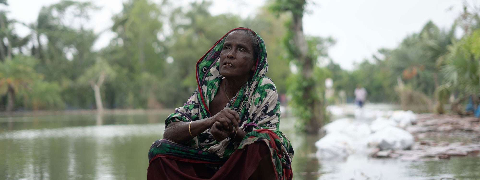 Woman in traditional dress sitting by floodwater in Bangladesh