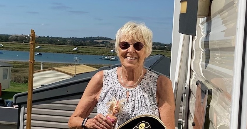 A lady with cropped hair stands smiling outside.