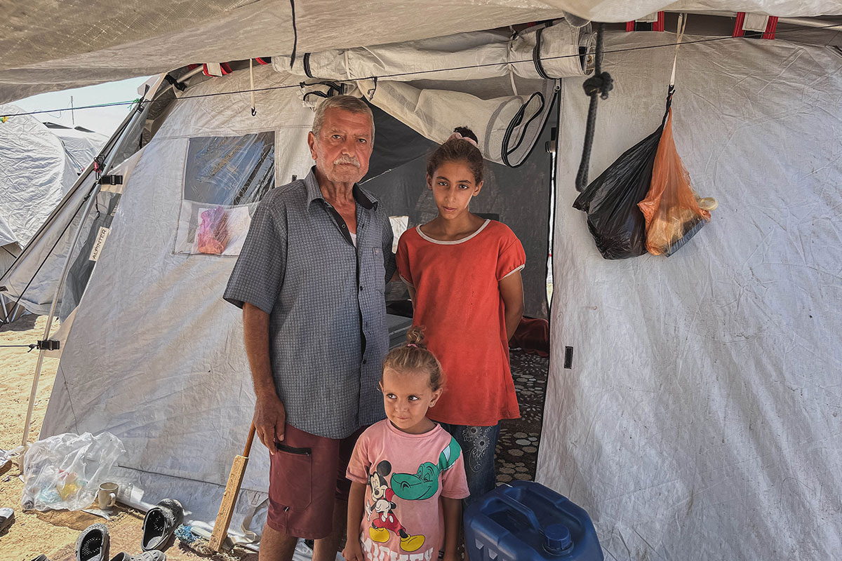 man stands with two daughters outside emergency tent